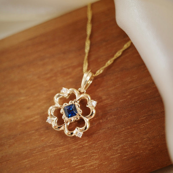 A gold clover pendant necklace with a central blue sapphire and small accent stone natural diamond. 
